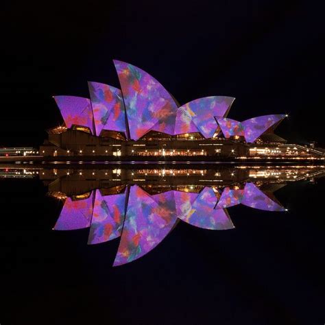 An Image Of The Sydney Opera Building Lit Up In Purple And Blue Lights At Night