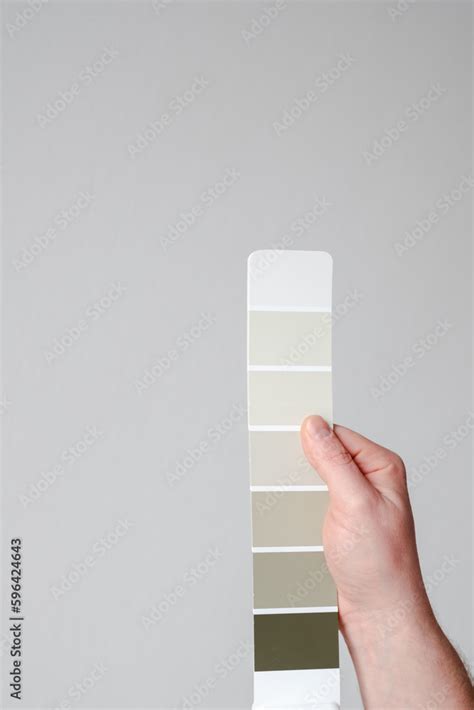 A man's hand holding off white color palette on a gray wall background ...