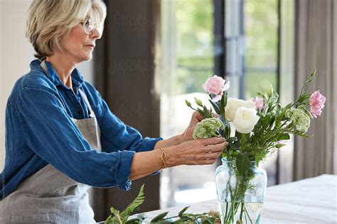 Senior Woman Arranging Flowers In Vase On Table Del Colaborador De