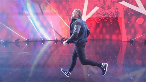 A Man Walking Across A Stage With Lights Behind Him