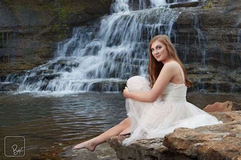 A Beautiful Woman Sitting On Top Of A Rock Next To A Waterfall In A