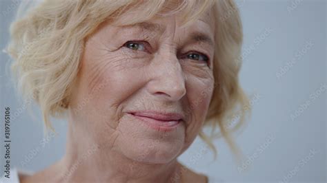 Beauty Portrait Of Stunning Blonde Old Woman With A Sincere Smile Against Grey Background