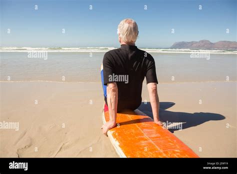 Rear View Of Senior Man Sitting On Surfboard At Beach Stock Photo Alamy