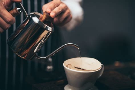 Barista despejando água quente da chaleira sobre o pó de café para