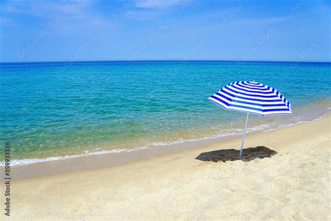 Striped blue and white sun umbrella on a white sand beach with emerald ...