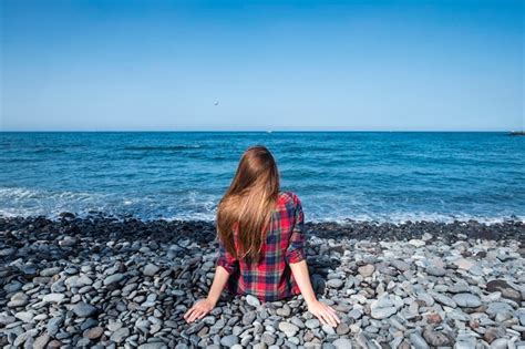 Premium Photo Rear View Of Woman Sitting On Rocks At Beach Against Sky