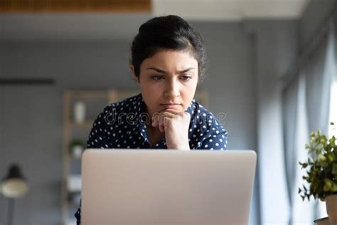 Head Shot Concentrated Young Indian Woman Looking At Laptop Monitor