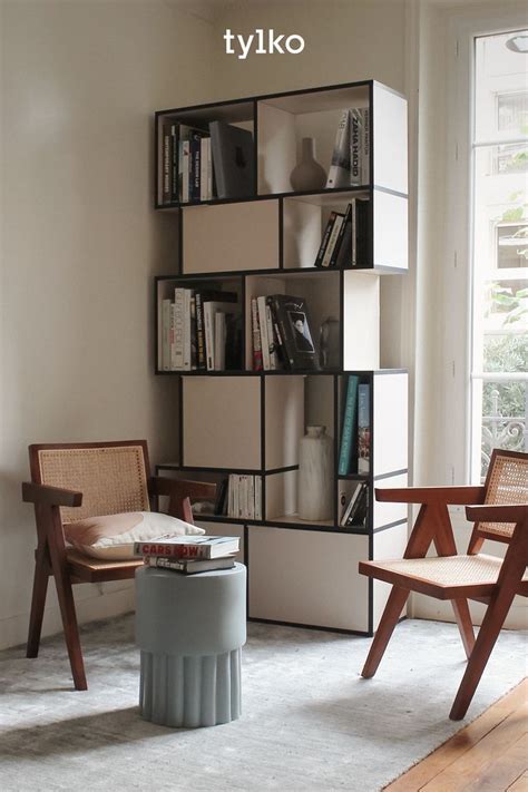 A Living Room With Two Chairs And A Book Shelf On The Wall Next To A Window