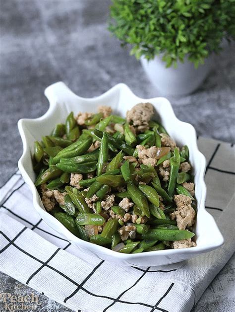 A White Bowl Filled With Green Beans And Meat On Top Of A Table Next To