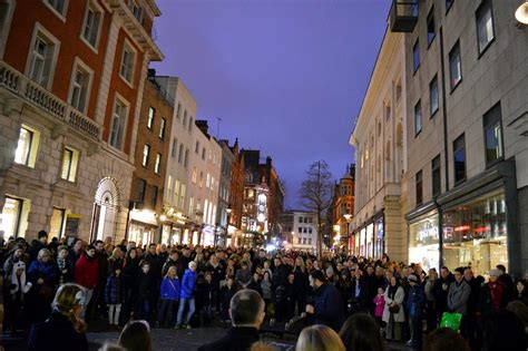 A Crowd Of People Standing On The Side Of A Street Next To Tall