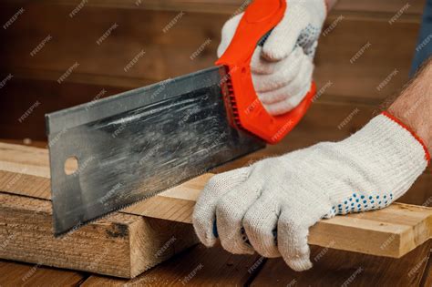 Premium Photo | A male carpenter using a hand saw saws a board