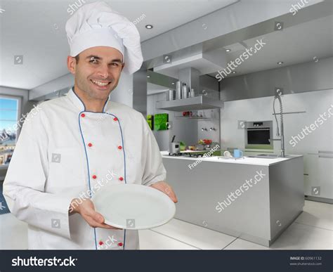 Smiling Chef Holding An Empty Plate In A Modern Kitchen Stock Photo