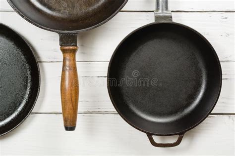 Several Empty Cast Iron Frying Pans On A White Wooden Background View