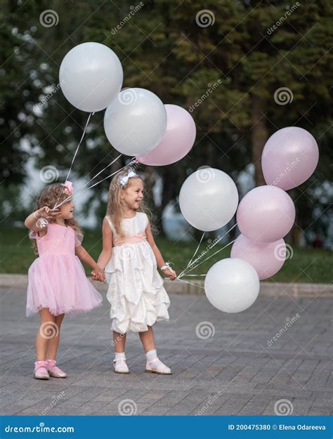 Two Little Girls in Pink and White Dressses with Balloons Walking on