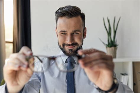 Smiling Businessman Looking At Pair Of Eyeglasses In Hands Stock Image