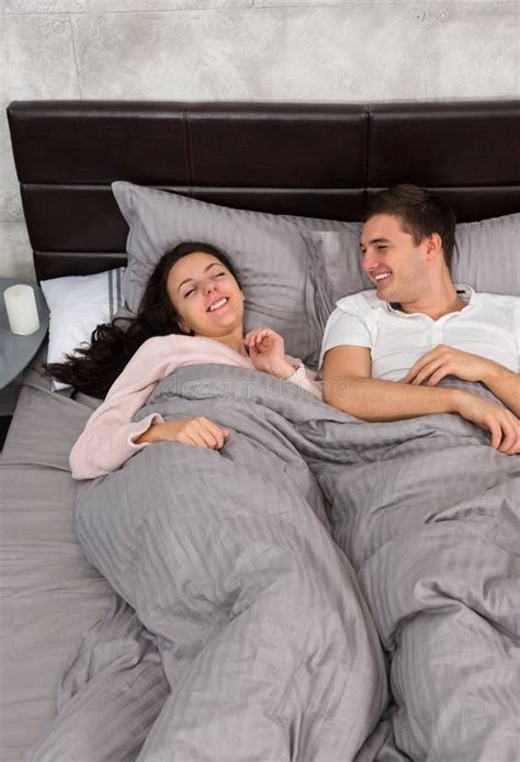 Young Couple Laughing And Wearing Pajamas While Lying In The Bed Stock