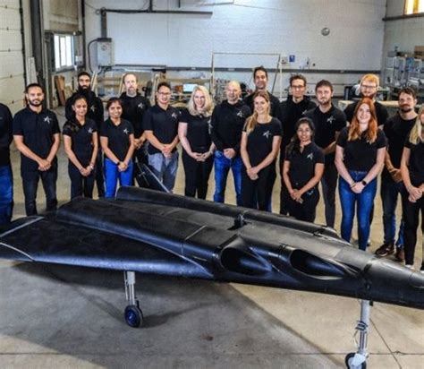 a group of people standing in front of a black jet model with two men and one woman