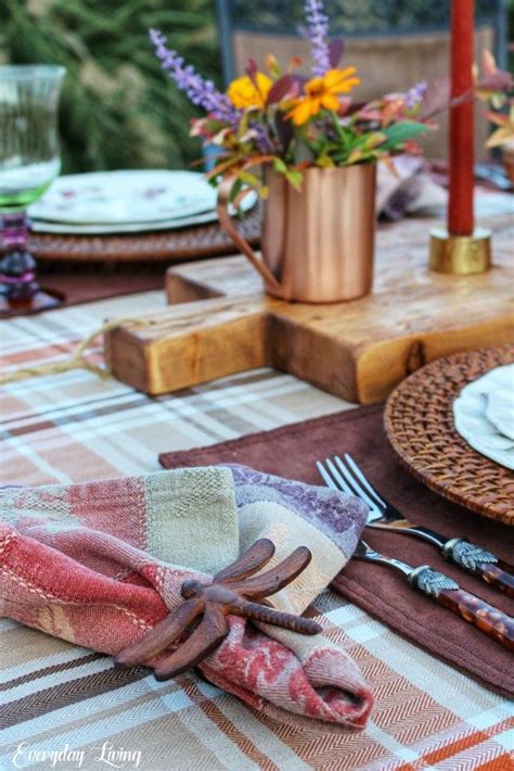 An Outdoor Table Set With Place Settings And Flowers In Copper Vases On