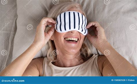 Happy Smiling Mature Woman Wearing Sleeping Mask Lying In Bed Stock