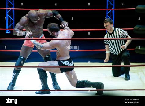 Two Male Professional Wrestlers Grappling In The Ring Beside A Referee