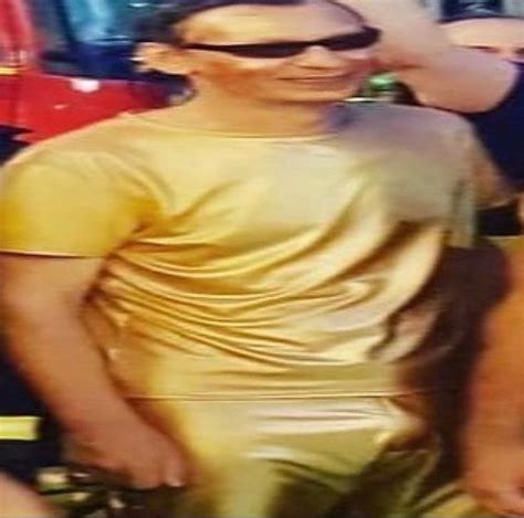 A Man In Gold Shirt And Sunglasses Standing Next To Other People