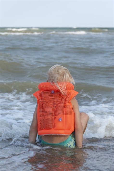 Kind Dat In Een Oranje Opblaasbaar Zwemvest Op De Kust Staat Verticaal