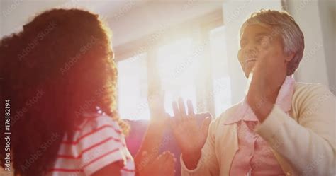 Granddaughter And Grandmother Playing Clapping Games On Sofa In Living