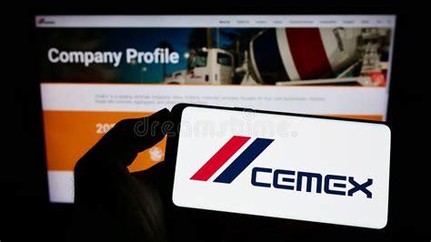 Person Holding Smartphone With Logo Of Mexican Materials Company CEMEX