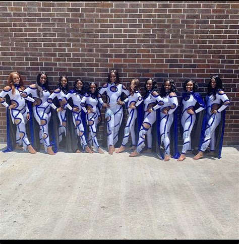 a group of women standing next to each other in front of a brick wall wearing white and blue outfits