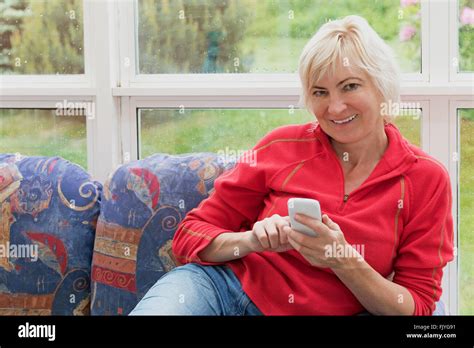 Smiling Blonde Middle Aged Woman Is Sitting On A Sofa And Is Looking To The Camera Stock Photo