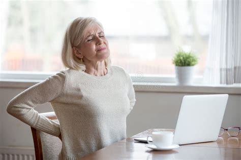 Blond Mature Lady Sitting On Bed And Touching Her Back Radiculitis And