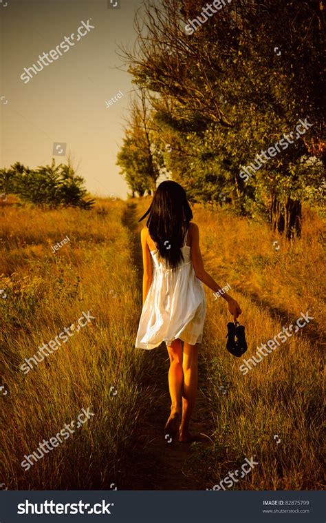 The Barefoot Girl In White Dress With Shoes In Hand Is On The Field