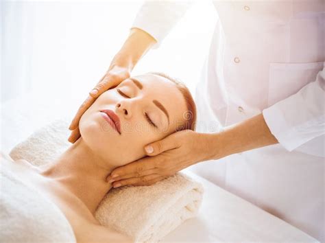 Beautiful Woman Enjoying Facial Massage With Closed Eyes In Sunny Spa