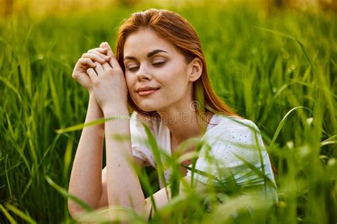 Portrait Of A Woman Sitting In The Grass With Her Hands Folded To Her