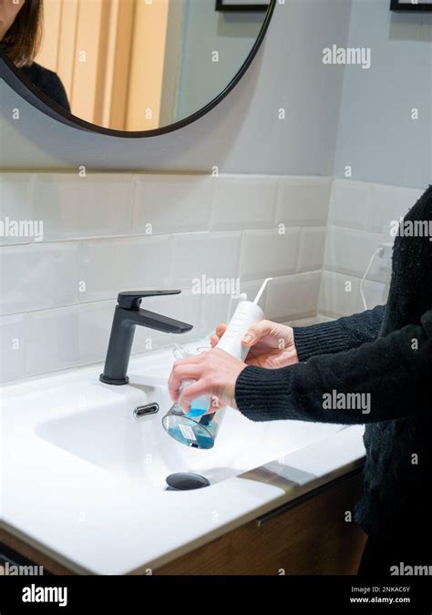 Effortless Oral Health Woman Filling Water Flosser Tank With Mouthwash At Bathroom Basin Stock