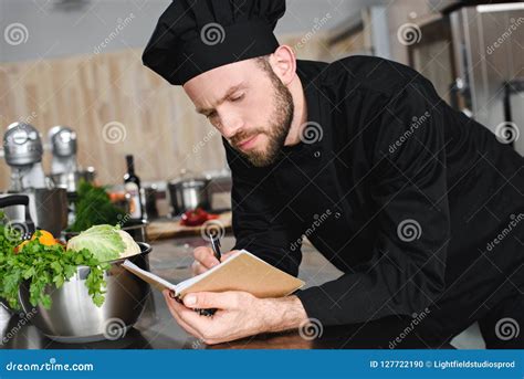 Side View Of Handsome Chef Writing Down New Recipe To Notebook Stock