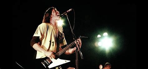 A Man With Long Hair And Beard Playing Guitar In Front Of A Microphone