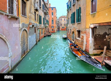 Gondola Floats On Small Canal Among Old Colorful Houses In Venice