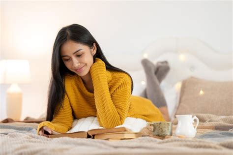 Premium Photo An Attractive And Relaxed Asian Woman In A Cosy Knitted Sweater Is Reading A