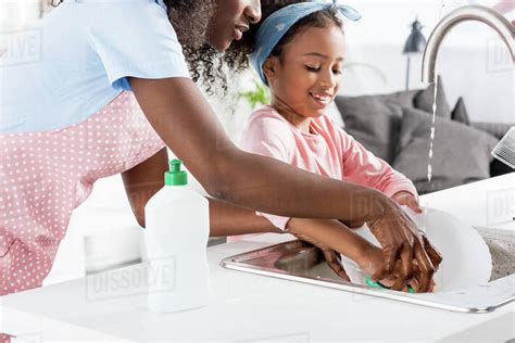 African American Mother And Daughter Washing Dishes With Detergent On