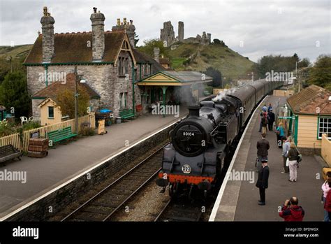 A Steam Train At Corfe Castle Railway Station With Corfe Castle In