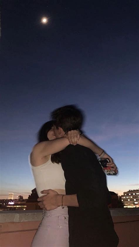 Two People Embracing Each Other While Standing On A Roof With The City