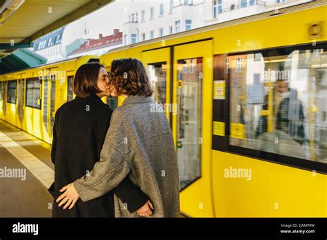 Lesbian Couple Kissing While Standing By Yellow Train At Railroad