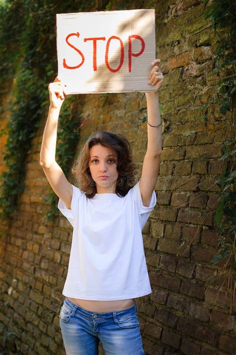 Young Protesting Woman In White Shirt And Jeans Holds Protest Sign