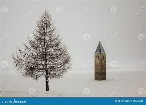 Beautiful Shot of Church Tower Near a Tree in Lake Reschen Covered with Snow in South Tyrol ...