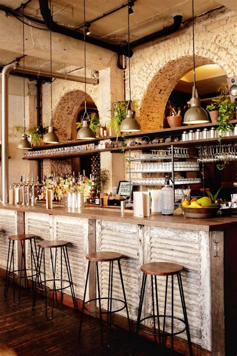 A Bar With Several Stools In Front Of It And Potted Plants Hanging From