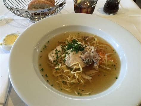 A Bowl Of Chicken Noodle Soup Sits On A Table With Bread And Water Glasses