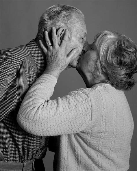 An Older Couple Kissing Each Other While Standing Next To Each Other In