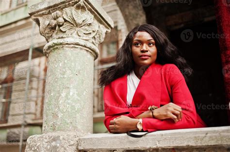 Stylish african american woman in red coat posed against old columns ...