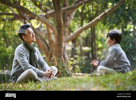 Asian Father And Son Sitting On Grass Having A Pleasant Conversation